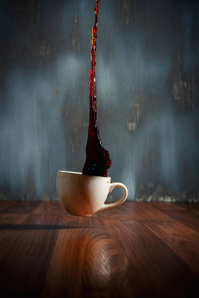 чашка горячего кофе проливая на деревянный пол и кофе брызги воды на темном фоне - Фото, изображение