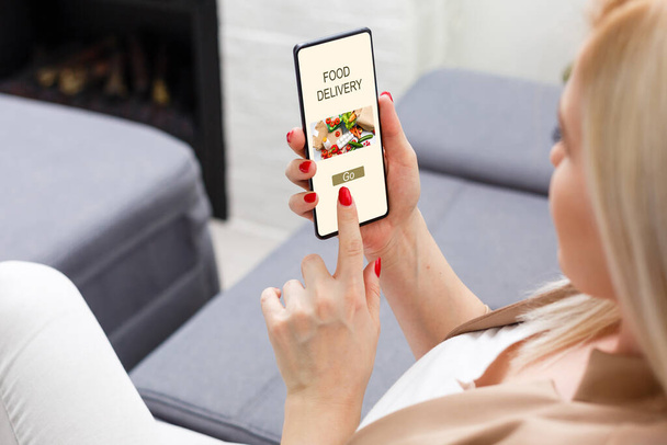 Menina encomendar pizza on-line no smartphone, com mesa e café e planta em segundo plano - Foto, Imagem