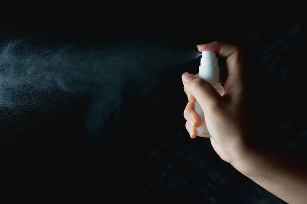 close up woman handing small spray bottle and spraying on dark background - Фото, зображення
