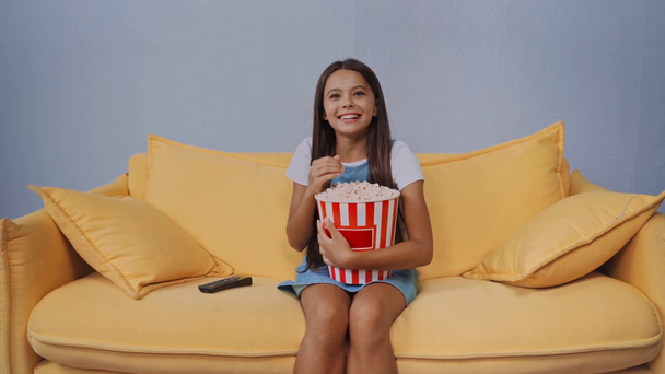 dítě sedí na gauči, dívá se na film a jí popcorn  - Záběry, video