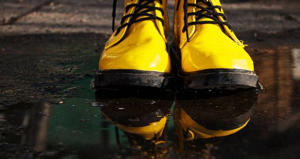 Botas de borracha amarelas brilhantes em pé em uma poça. Botas com uma sola maciça de um trator de cor preta. Conceito do tempo chuvoso A primavera chegou, o outono chegou. Escotilha em água. - Foto, Imagem