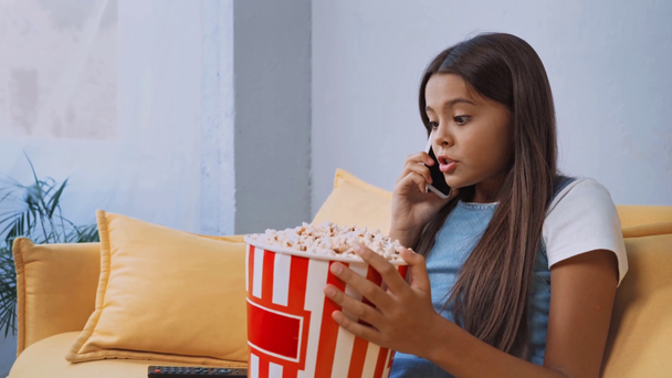 παιδί που μιλάει στο smartphone, βλέπει ταινία και τρώει ποπ κορν  - Πλάνα, βίντεο