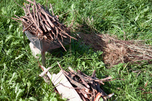 Metal grill with firewood among the green grass in the meadow. Near firewood and grass for lighting. - Zdjęcie, obraz