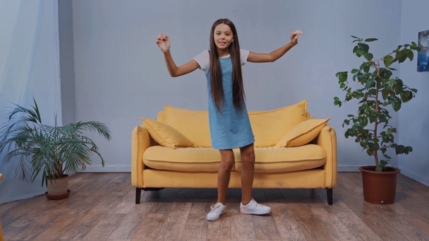 Kinder im Kleid tanzen neben Pflanzen und sitzen auf dem Sofa  - Filmmaterial, Video