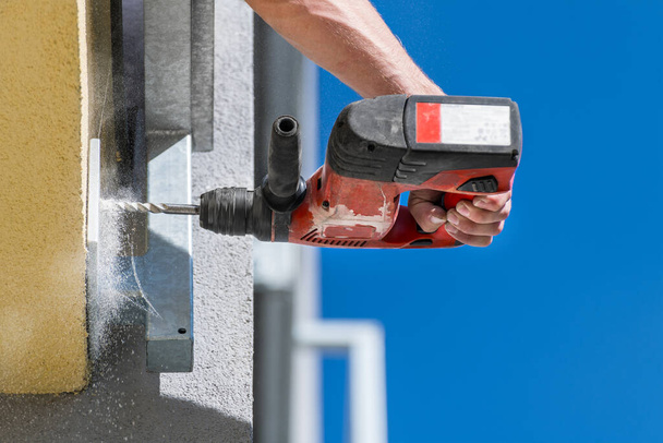 Working power hammer drill. Anchoring of steel construction into building masonry. Hand holding cordless drilling machine. Fixing and mounting of guard rail on terrace or balcony. Falling dust detail. - Photo, Image