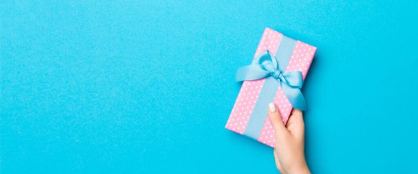 Γυναικεία αγκαλιά κρατώντας κουτί δώρου με χρωματιστή κορδέλα σε μπλε φόντο πίνακα, πάνω όψη και χώρο αντίγραφο για το σχεδιασμό σας. - Φωτογραφία, εικόνα