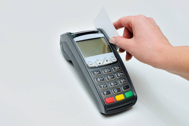 Το κορίτσι κρατά στο χέρι μια πιστωτική κάρτα μπροστά από το τερματικό σε λευκό φόντο. Μια λευκή πιστωτική κάρτα χωρίς εικόνα. Πληρωμή με πιστωτική κάρτα στο τερματικό - Φωτογραφία, εικόνα