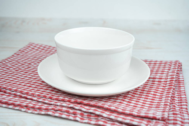 White empty ceramic bowl on a plate on a red kitchen plaid towel. - Zdjęcie, obraz