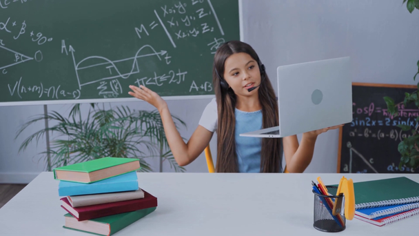 μαθήτρια με ακουστικά χαιρετώντας το χέρι ενώ σπούδαζε στο σπίτι στο διαδίκτυο - Πλάνα, βίντεο