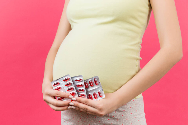 Zugeschnittenes Bild von Medikamenten in Blasen in den Händen von Schwangeren vor buntem Hintergrund mit Kopierraum. Einnahme von Vitamintabletten während der Schwangerschaft. - Foto, Bild
