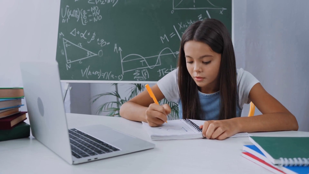 Schulkind schreibt in Notizblock, während es zu Hause E-Learning macht - Filmmaterial, Video
