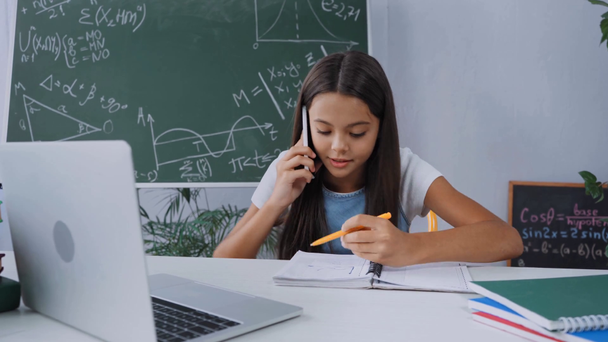 школярка говорить на смартфоні біля ноутбука і блокнотів на столі
 - Кадри, відео