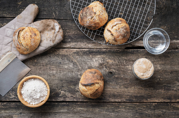 Top view a házi készítésű frissen sült kovászos kenyér zsemle, indító élesztő, víz és liszt rusztikus fa lapok. - Fotó, kép