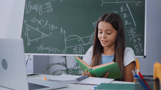Kind liest Buch neben Laptop und Notizbuch auf Schreibtisch vor - Filmmaterial, Video