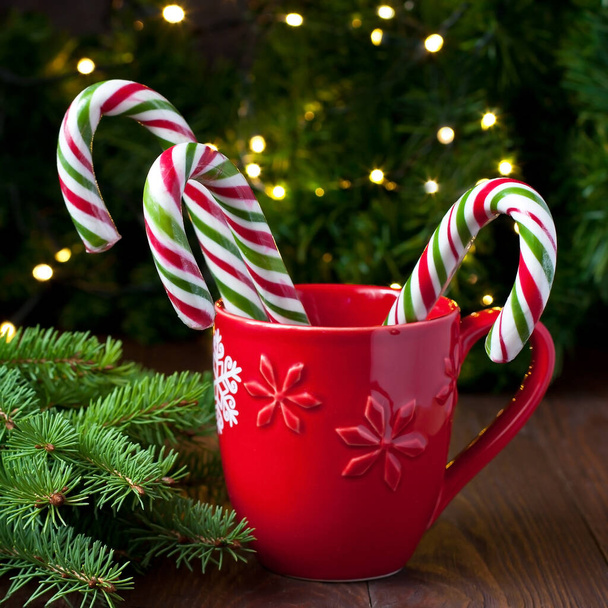 Bastones de caramelo de menta rayada roja y verde en taza de Navidad en mesa de madera - Foto, Imagen