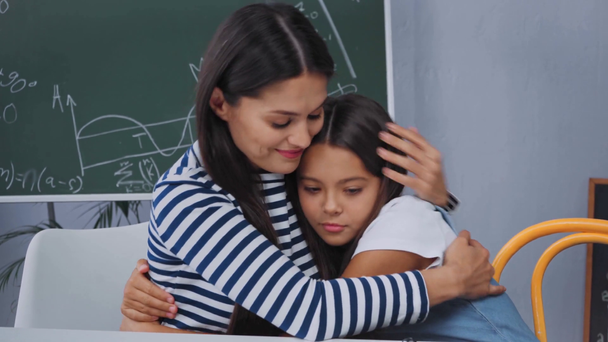 madre en calma y abrazo escolar molesto cerca del escritorio con cuadernos  - Metraje, vídeo
