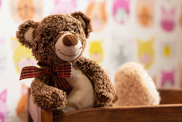 zachte bruine teddybeer zit in een kinderbed in een kinderkamer op een wazige achtergrond - Foto, afbeelding