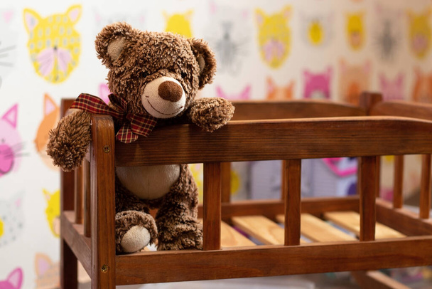 oso de peluche marrón suave se sienta en una cama de madera para niños en una habitación para niños sobre un fondo borroso - Foto, imagen