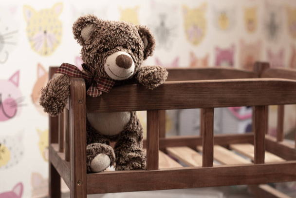urso de pelúcia marrom macio senta-se em uma cama de madeira infantil em um quarto de crianças em um fundo turvo - Foto, Imagem