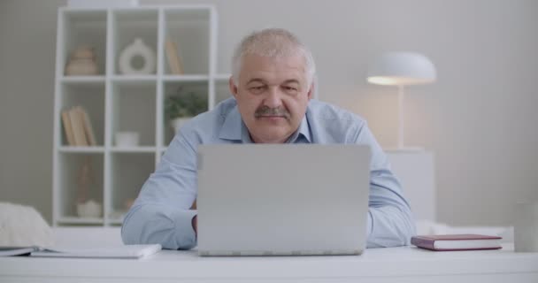 hombre anciano con bigote está trabajando con el ordenador portátil, sentado en la habitación, contestando en el correo electrónico, escribiendo el texto del mensaje, remotamente el trabajo desde casa - Imágenes, Vídeo