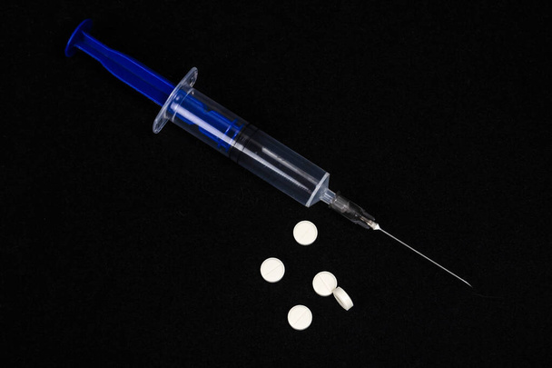Blue syringe with an open needle and white pills on a dark black background - Φωτογραφία, εικόνα
