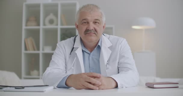 Online-Konsultation mit Facharzt, männlicher Arzt hört zu und nickt mit dem Kopf, mittleres Porträt in seinem klinischen Büro - Filmmaterial, Video