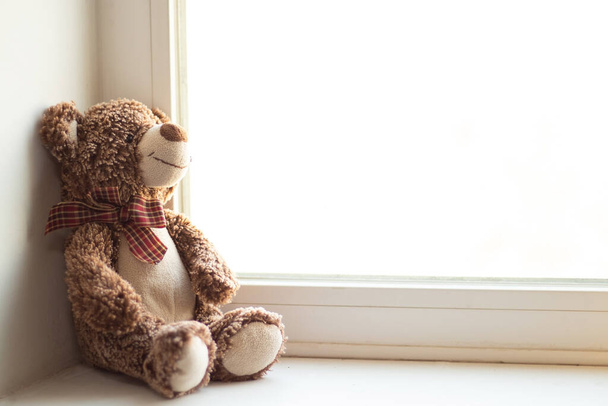 urso de pelúcia marrom senta-se na janela sozinho, brinquedo infantil - Foto, Imagem