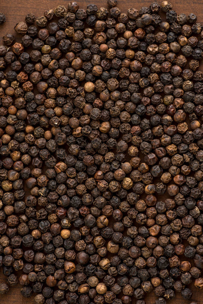 Close up of black pepper or peppercorns as background on wooden background. - 写真・画像