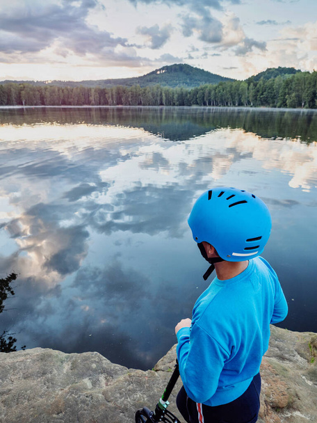 Rapaz bonito com capacete patinador azul chegou por empurrar scooter para o lago. Pôr do sol de verão no parque natural. - Foto, Imagem