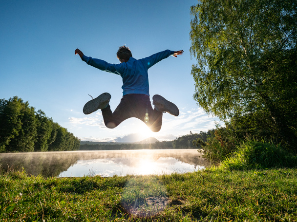 Szalony skaczący chłopiec świętuje wolność i zabawia się nad jeziorem. Szalone i niesamowite childood - Zdjęcie, obraz