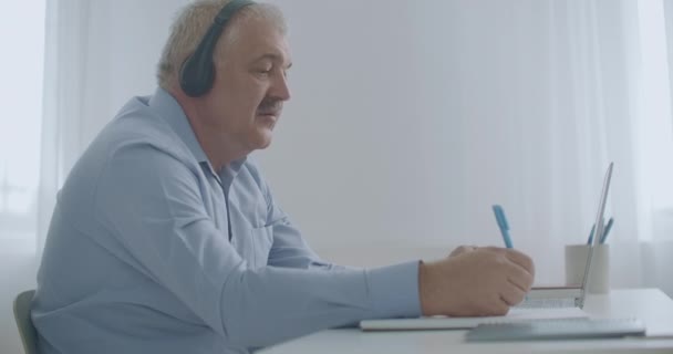 aged male lawyer is consulting client by internet, using online chat in laptop, writing notes and speaking - Footage, Video
