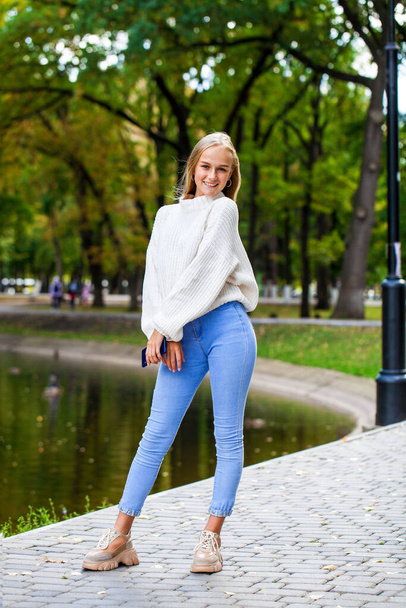 full length portrait of a young girl in blue jeans and a woolen sweater, autumn park outdoor  - Valokuva, kuva