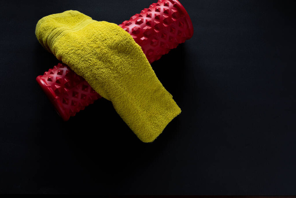 κόκκινο roller γυμναστήριο και ένα πράσινο πετσέτες σε μαύρο σπίτι γυμναστήριο φόντο - Φωτογραφία, εικόνα