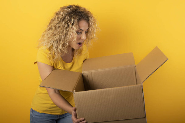 Happy woman receives a package from online shop order. Yellow background. - Фото, зображення