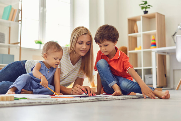 Young mommy and children drawing picture together sitting on floor in nursery - Fotoğraf, Görsel