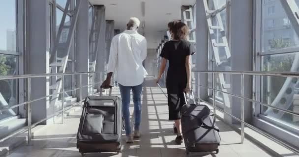 Вид сзади на африканскую пару, идущую вместе в аэропорт в отпуск. Путешествовать вместе. Несите рюкзак и чемоданы. Привлекательная молодая женщина и мужчина с чемоданами готовы к путешествию - Кадры, видео