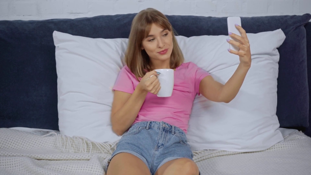 молода жінка бере селфі з чашкою кави в ліжку
 - Кадри, відео