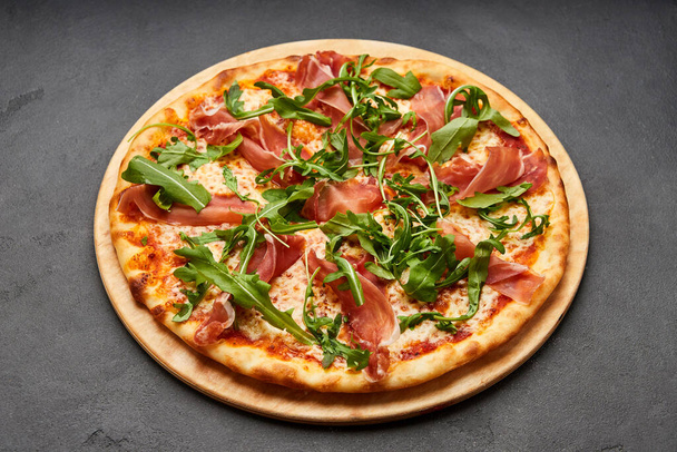Delicious Italian Pizza with Parma ham and arugula, mozzarella cheese on dark background - Photo, Image