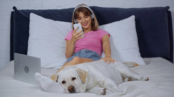 szelektív fókusz a kutya feküdt közelében nő fülhallgató zenét hallgatni - Felvétel, videó