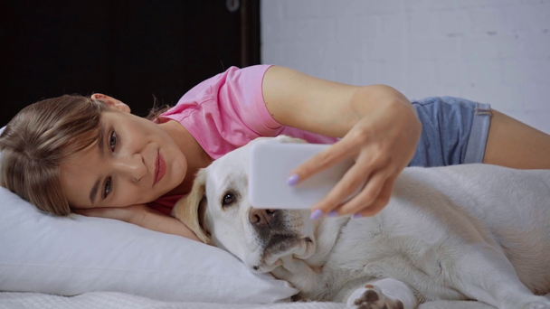 donna soddisfatta sdraiata sul cuscino e scattare selfie con golden retriever - Filmati, video