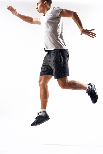 Sportler in Turnschuhen, kurzer Hose und T-Shirt auf hellem Hintergrund und in vollem Wuchs zur Seite laufend - Foto, Bild