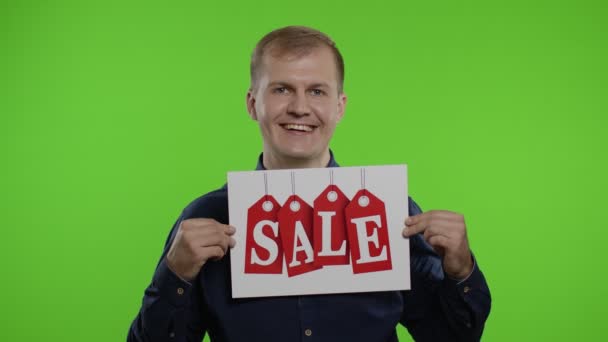 Μεγάλες εκπτώσεις. Ευτυχισμένος χαρούμενος ξανθός άνδρας σε μπλε πουκάμισο δείχνει λέξη πώληση επιγραφή διαφήμιση - Πλάνα, βίντεο