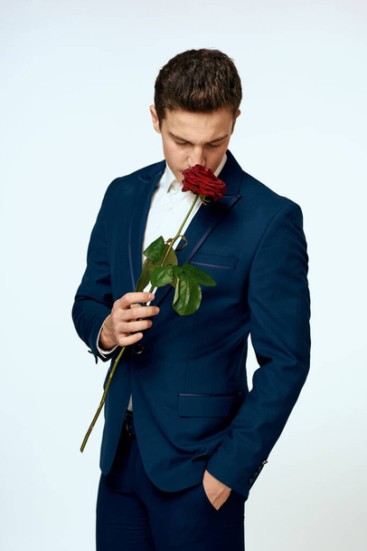 A man in a suit with a rose in his hands a gift date light background - Φωτογραφία, εικόνα