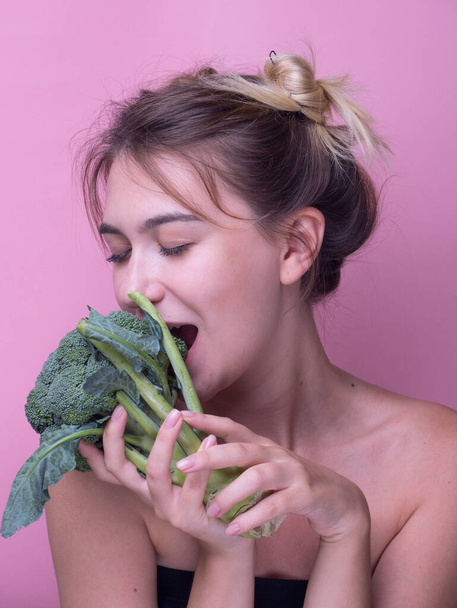 若い女性は大きな新鮮なブロッコリー人参野菜をかむ。ピンクの背景の女性に隔離された食事の健康的な食事の概念は緑ブロッコリーを食べる。生食だ。ビーガンフード。パノラマ - 写真・画像