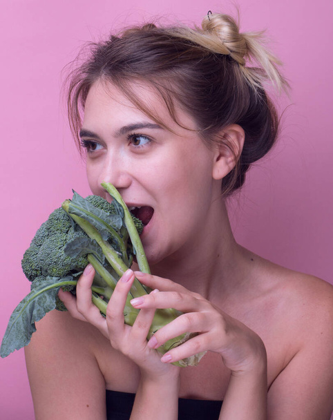 Fiatal nő harap nagy friss brokkoli sárgarépa zöldség. Diéta egészséges táplálkozás koncepció elszigetelt rózsaszín háttér nő eszik zöld brokkoli. nyers étel. Vegán kaja. panoráma - Fotó, kép