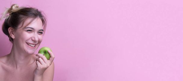 Portret wesołej młodej kobiety jedzącej zielone jabłko na różowym tle. Zdrowe zęby. Piękna dziewczyna z doskonałym białym zębem Holding czerwone jabłko Uśmiechnięta pozowanie na różowym tle Studio. - Zdjęcie, obraz