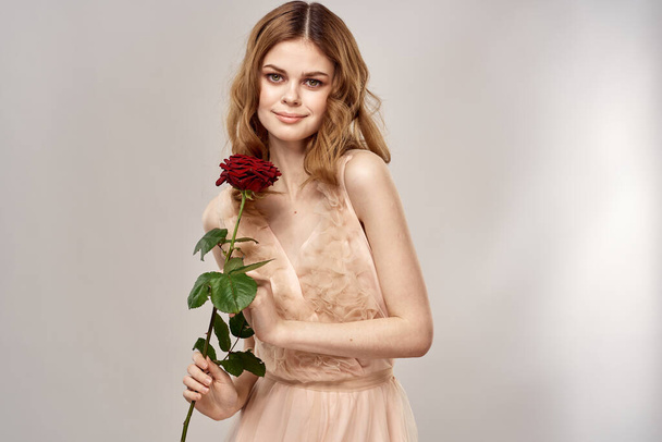 Retrato de uma mulher bonita com uma rosa vermelha em um fundo bege vista cortada de um vestido de noite - Foto, Imagem