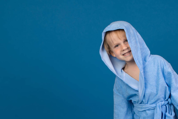 A child in a bathrobe playfully peeks out from the right against a blue background. Close-up studio shot with space for text for pool, spa, sauna and bath wash. - Photo, Image