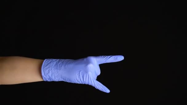 Női kéz egy latex orvosi kesztyű teszi a rock gesztus elszigetelt fekete háttér - Felvétel, videó
