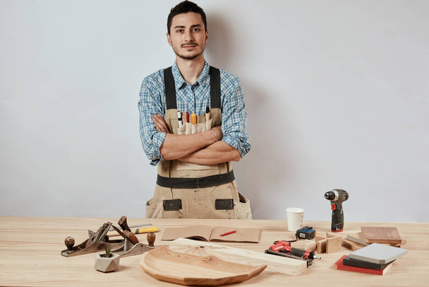 Confident young woodworker standing next to workbench in his carpentry workshop - Foto, Bild